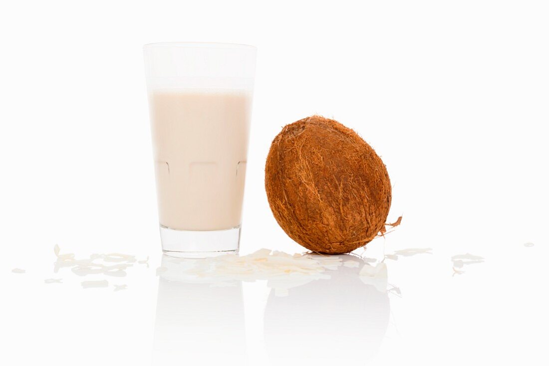 A glass of coconut milk with coconut and grated coconut next to it