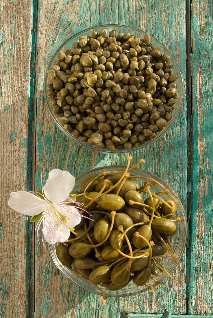 Capers and caper fruits in glass bowls (seen from above)