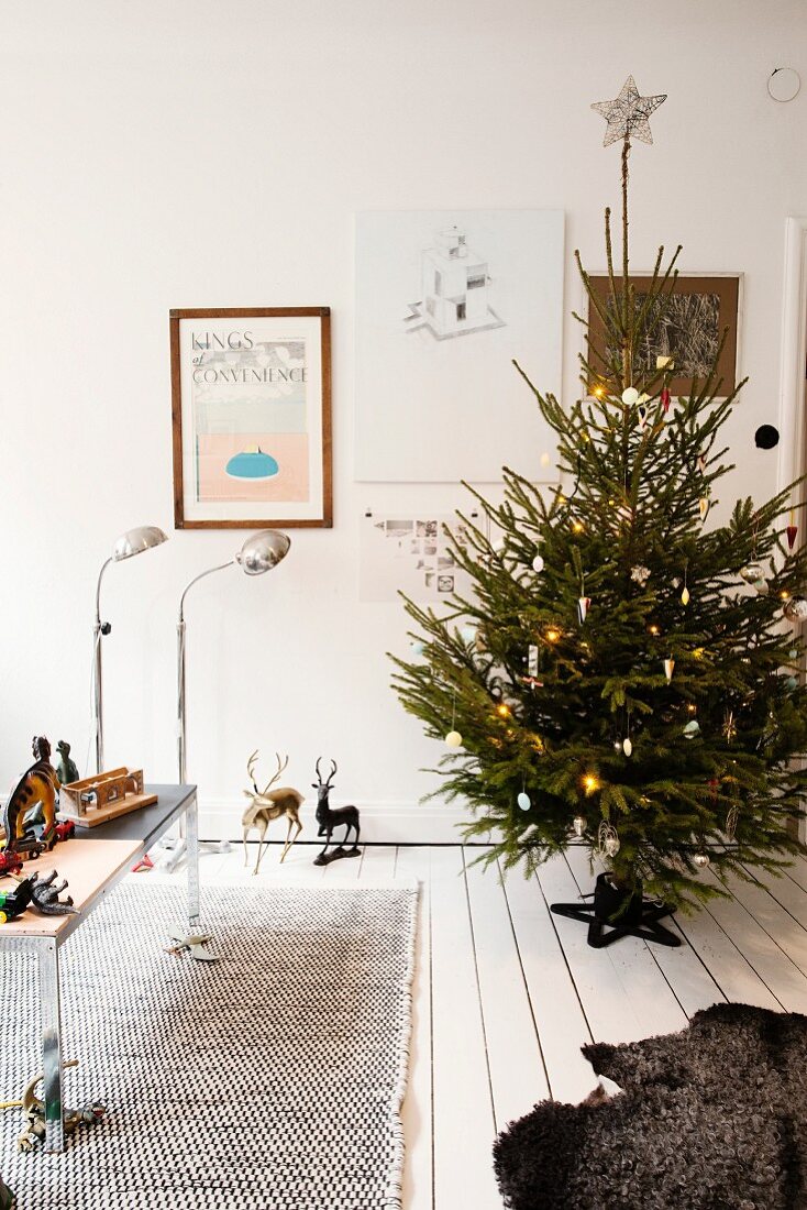 Geschmückter Weihnachtsbaum auf weißem Dielenboden, Tisch mit Spielzeugfiguren vor Retro Stehleuchten