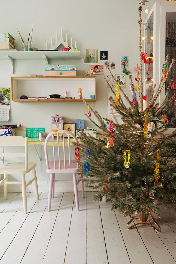 Decorated Christmas tree next to desk and wooden chair below wall-mounted shelves