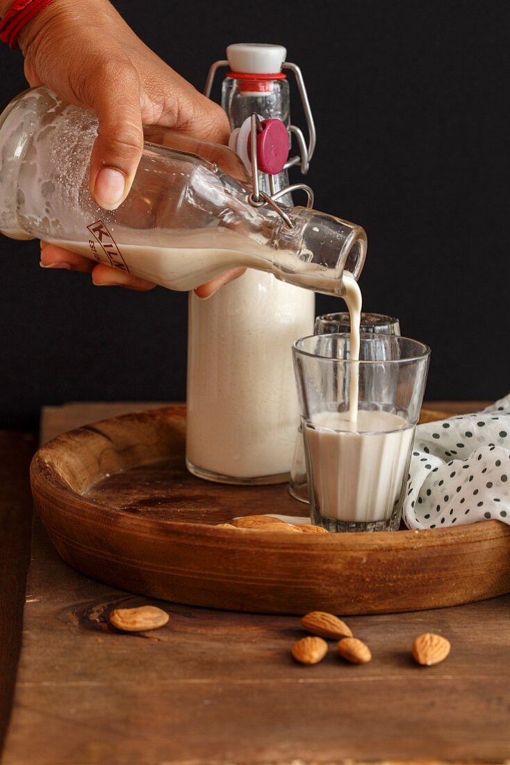 Homemade almond milk being poured from a flip-top bottle into a glass