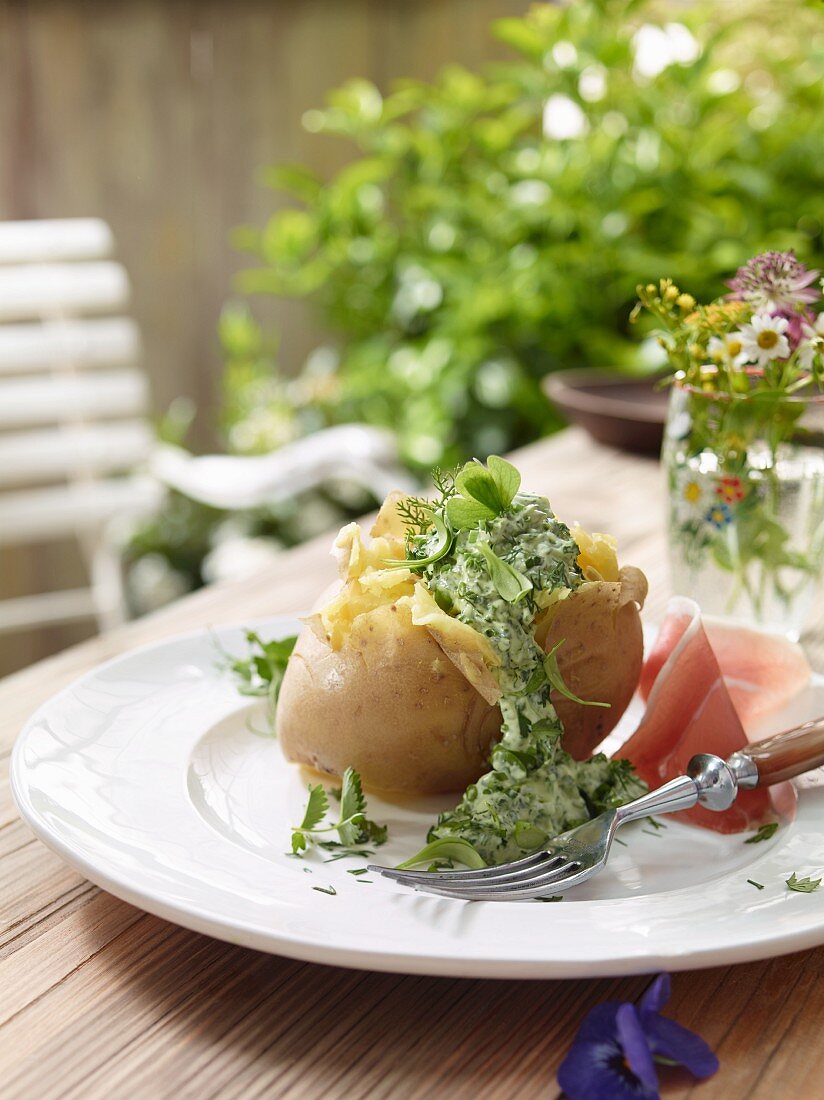 Ofenkartoffel mit Kräutersauce auf Gartentisch im Freien