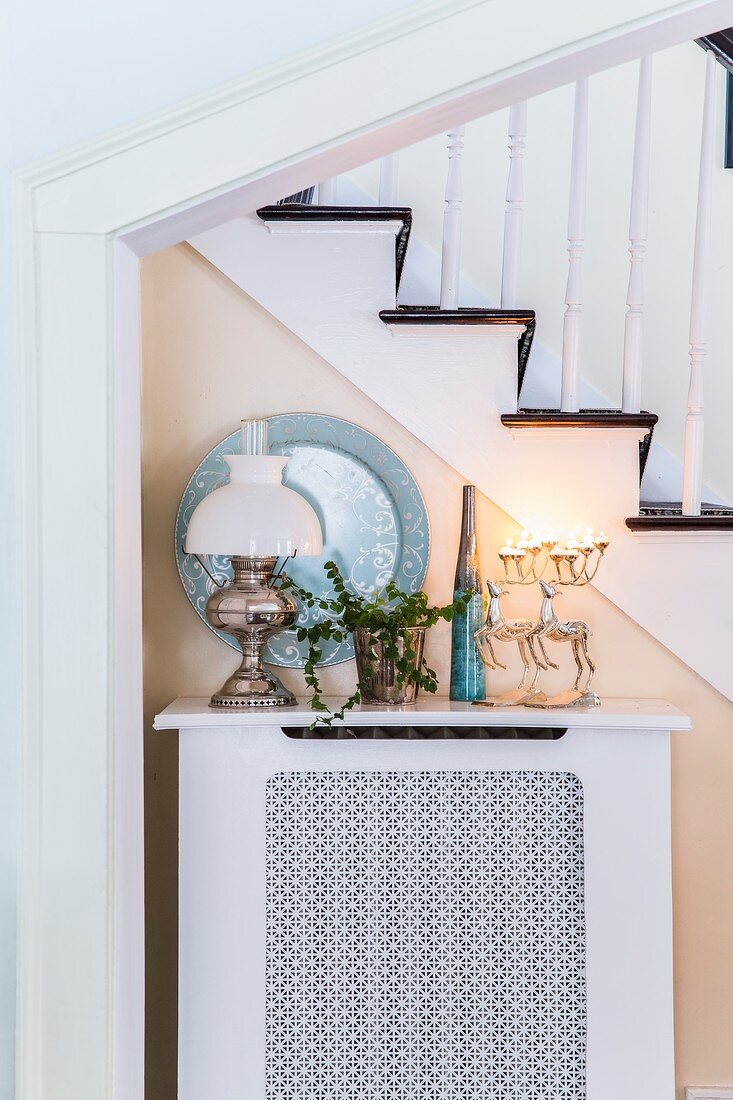 Stag-shaped candelabr and ceramic and classic oil lamps on top of radiator cover against side of staircase