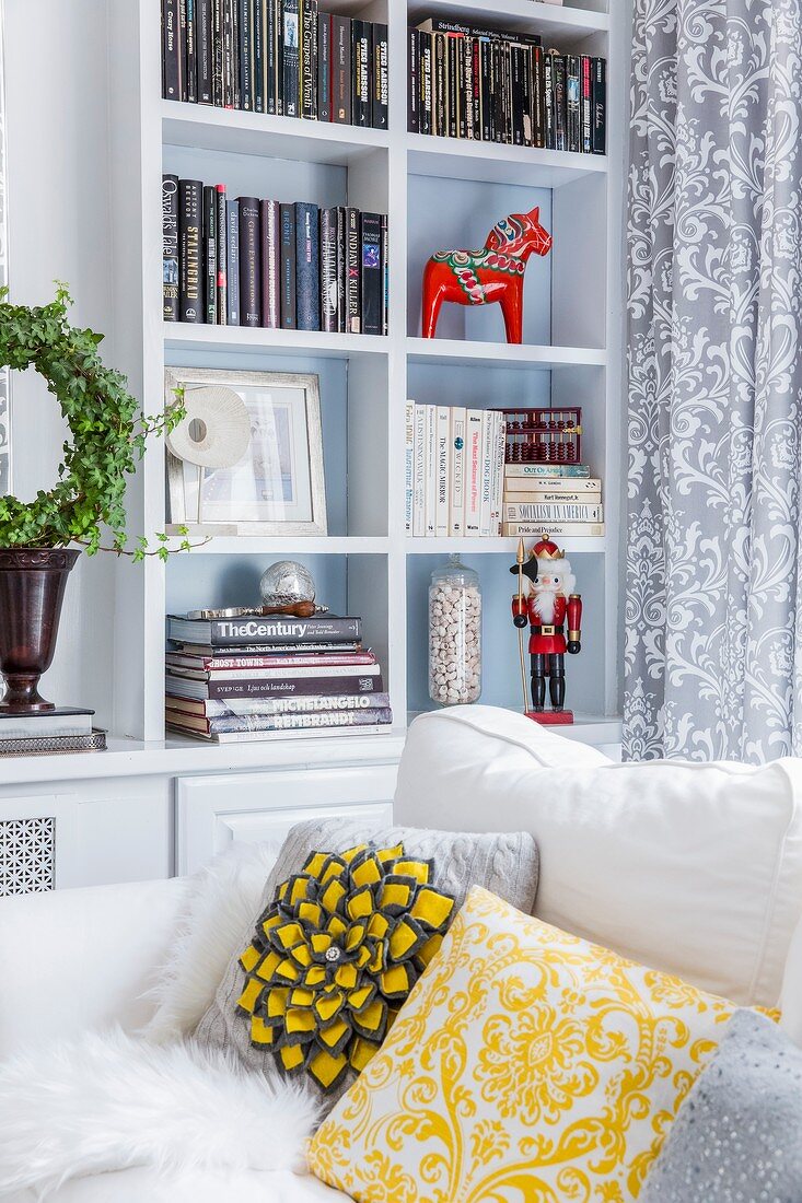 Red Advent horse figurine and nutcracker in white shelving compartments behind white sofa with yellow and grey scatter cushions
