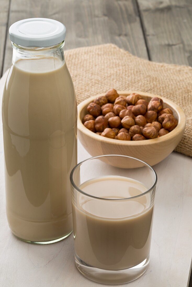 Haselnussdrink im Glas und in der Flasche mit Haselnusskernen in der Schale