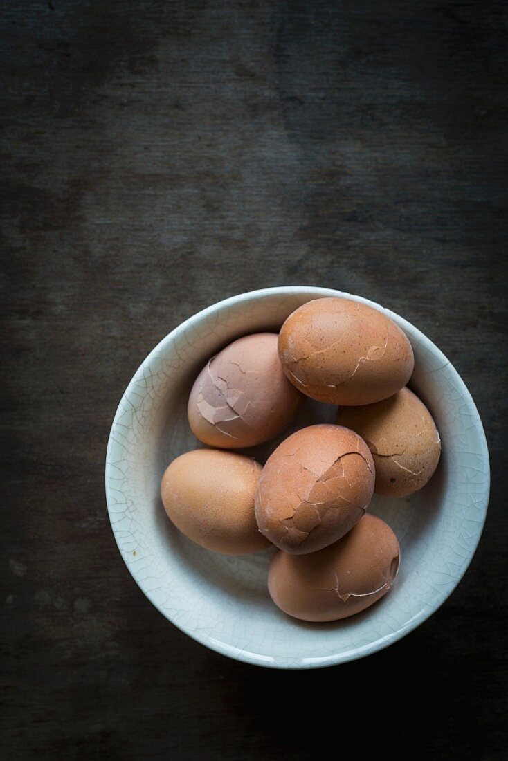 Angestossene Eier für Soleier in Keramikschale auf Holztischplatte