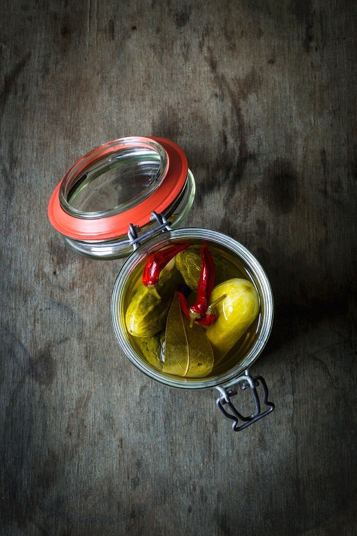 Gherkins with chillis in a preserving jar on a wooden table