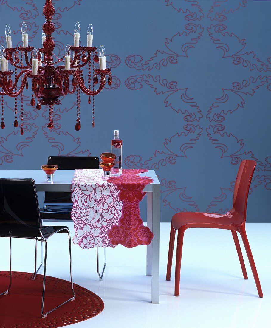 Red chandelier above table with patterned runners in front of blue wall with ornate pattern