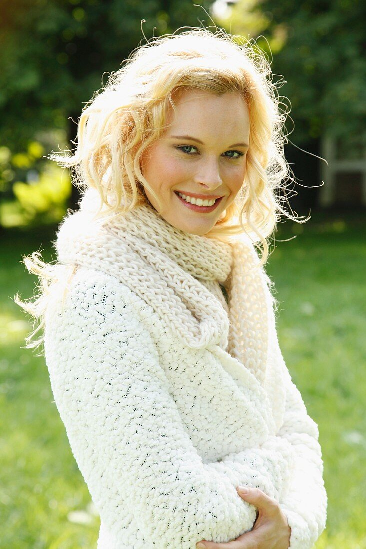 A young woman wearing a white, coarse-knit cardigan and scarf