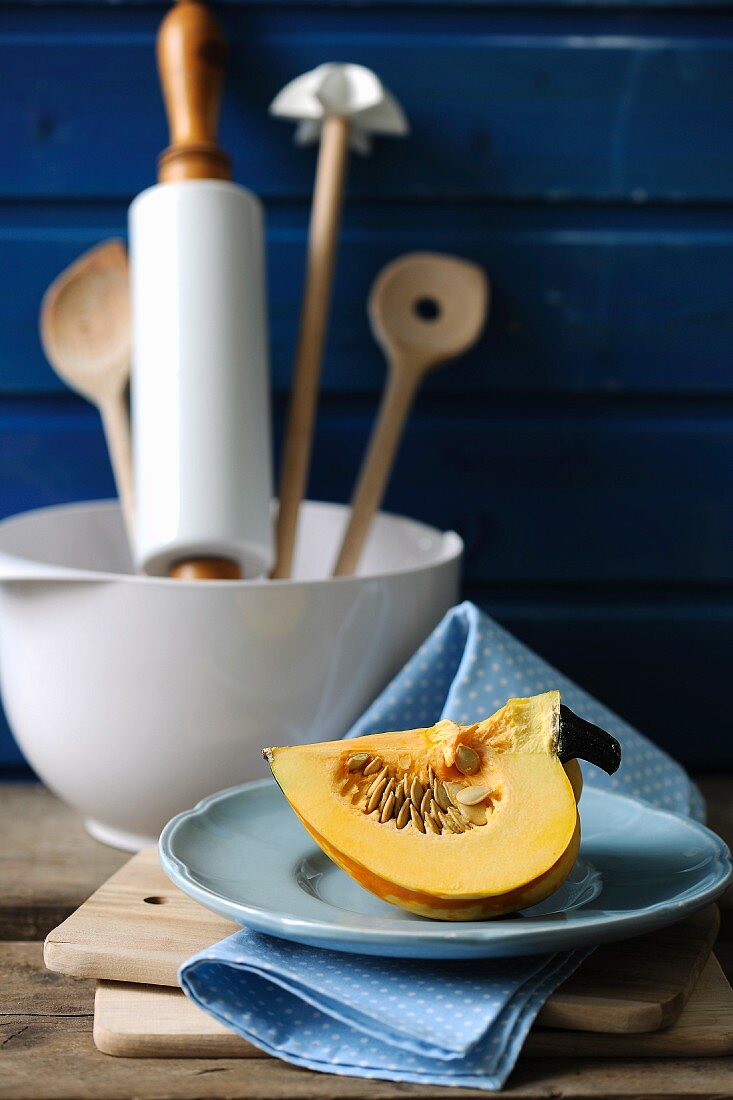 A pumpkin wedge on a plate with various kitchen utensils in the background