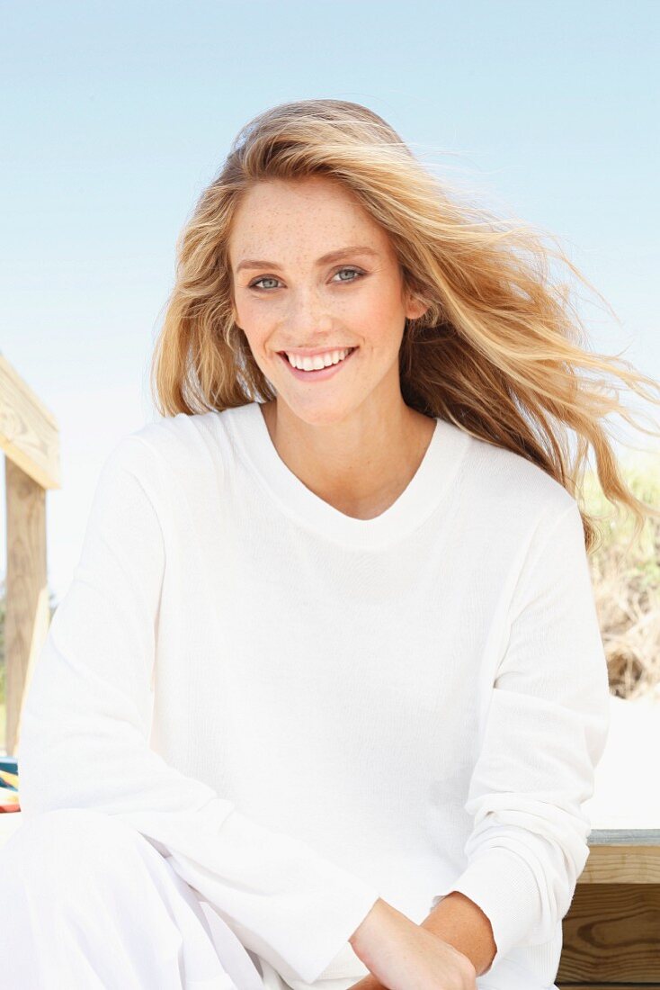 Junge Frau in weißem Langarmshirt und Hose am Strand