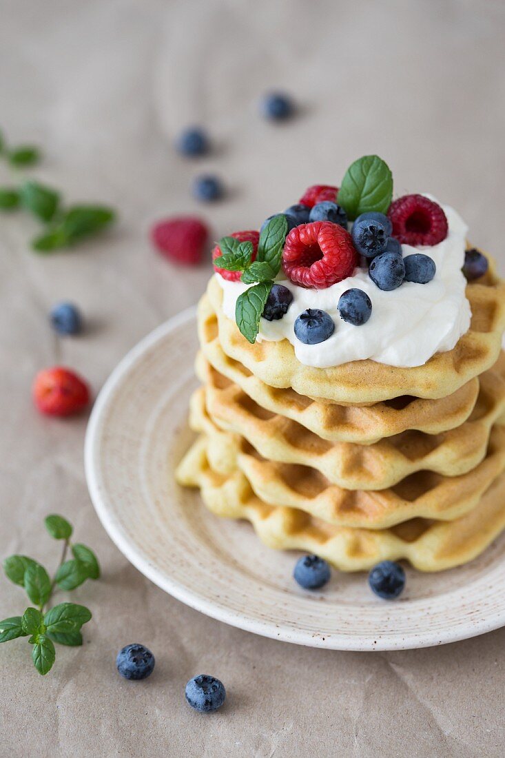 A stack of waffles with raspberries, blueberries and whipped cream