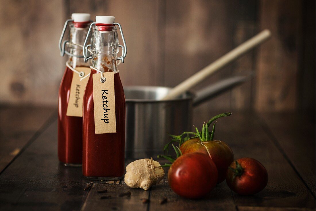 Bottle of homemade ketchup with ingredients and kitchen utensils on a wooden table