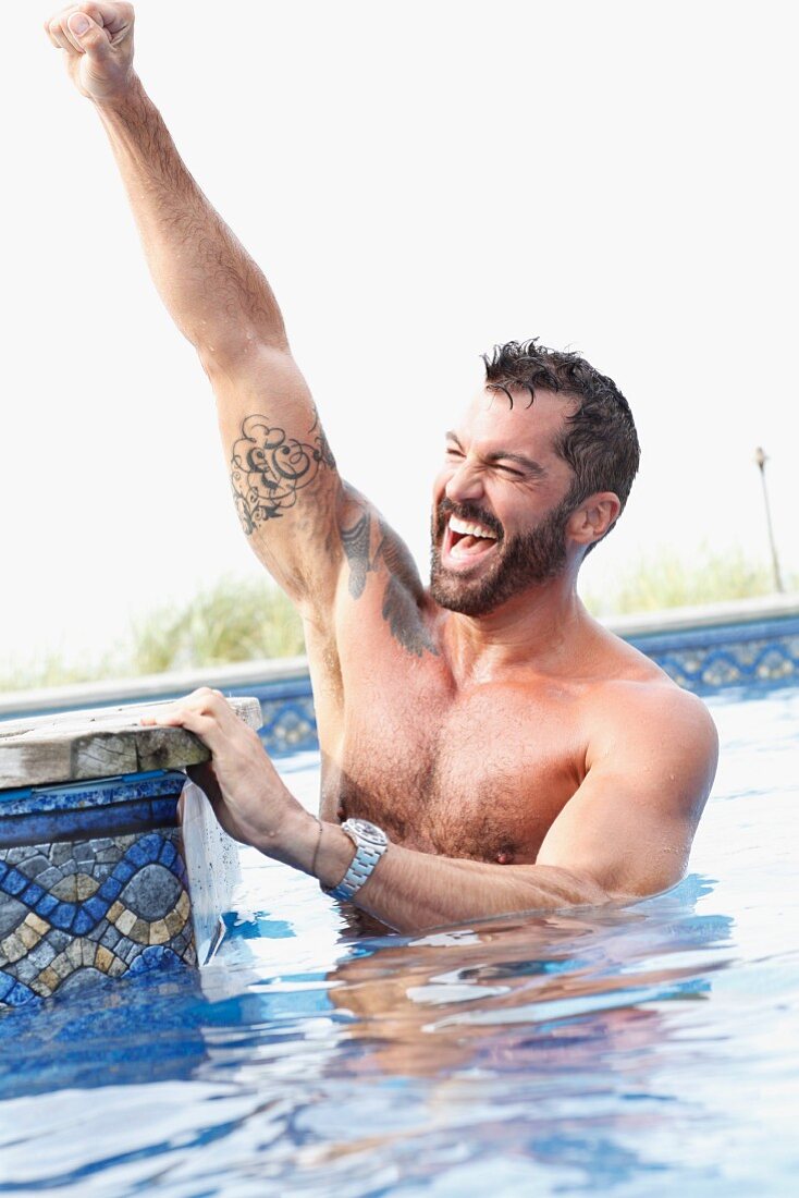 A dark-haired man with a beard cheering in a pool