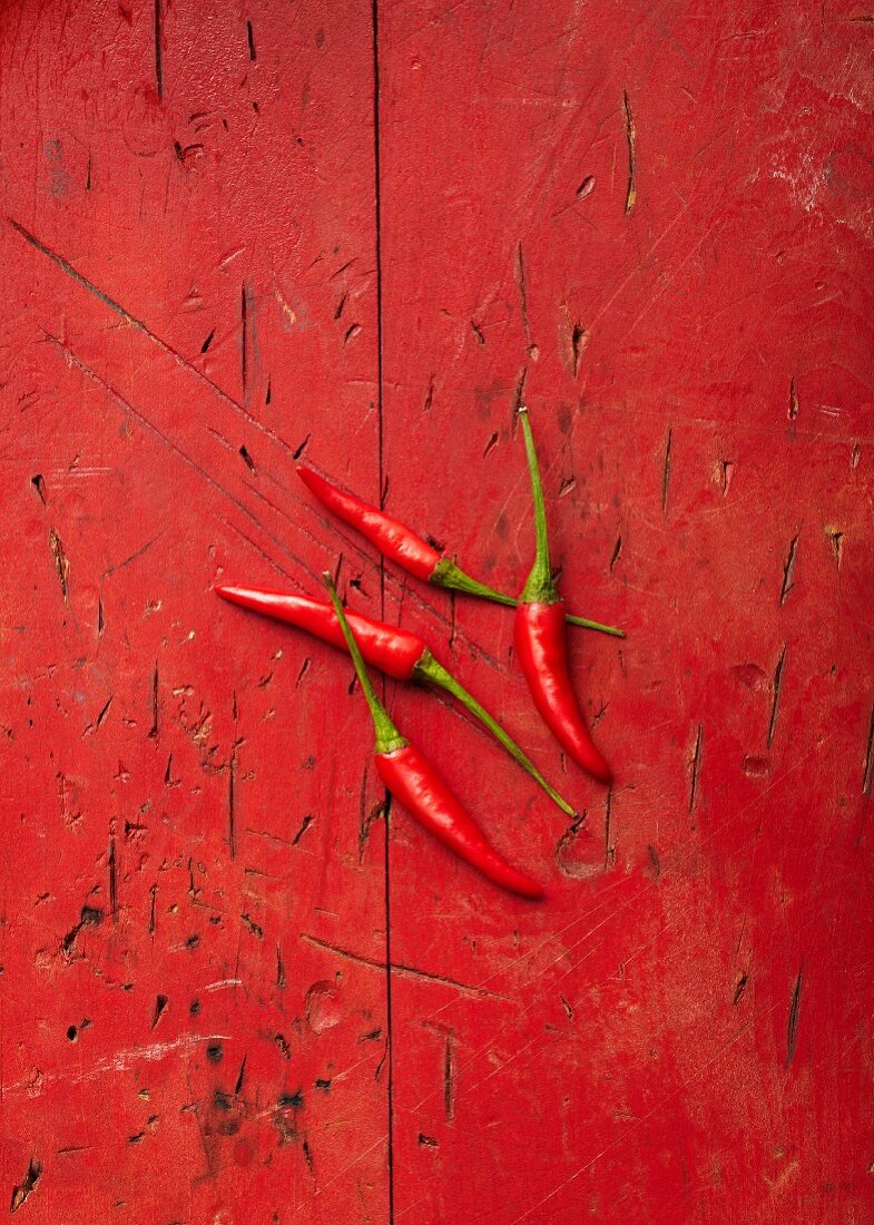 Four red Bird's Eye chillis on a red surface