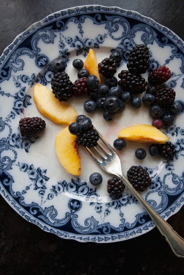 Pfirsiche, Brombeeren und Heidelbeeren auf blau-weiss gemustertem Teller mit Gabel