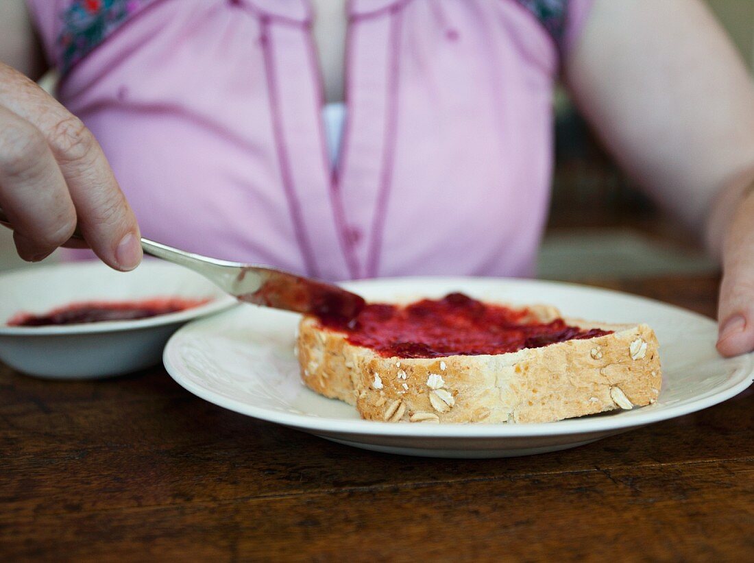 A woman spreading strawberry jam onto a slice of toast