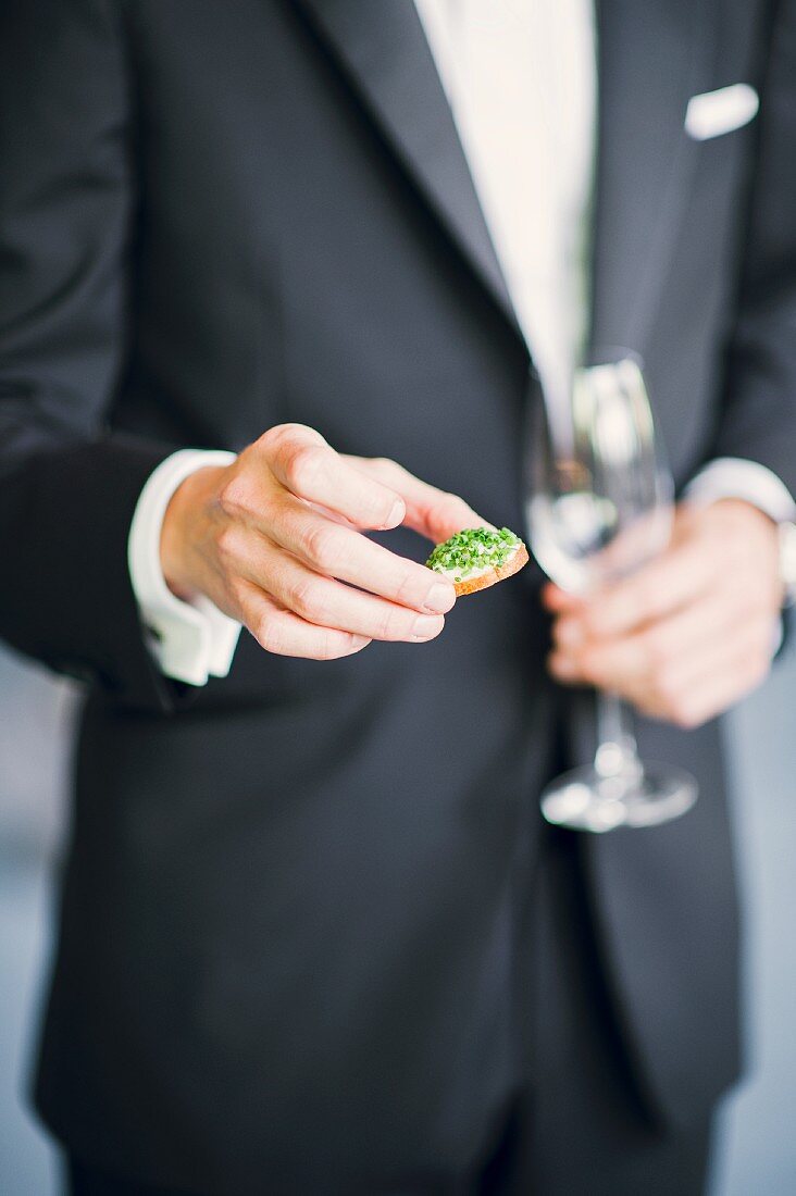 A bride groom holding a canapé and a glass of champagne