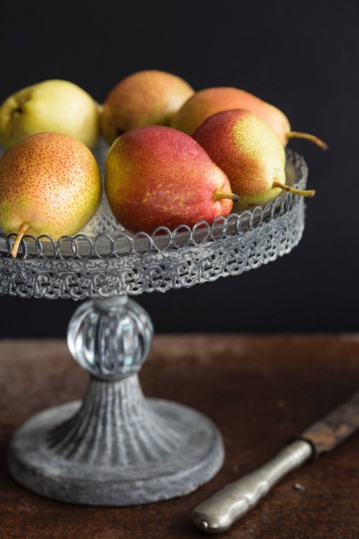 Pears on a cake stand against a black surface