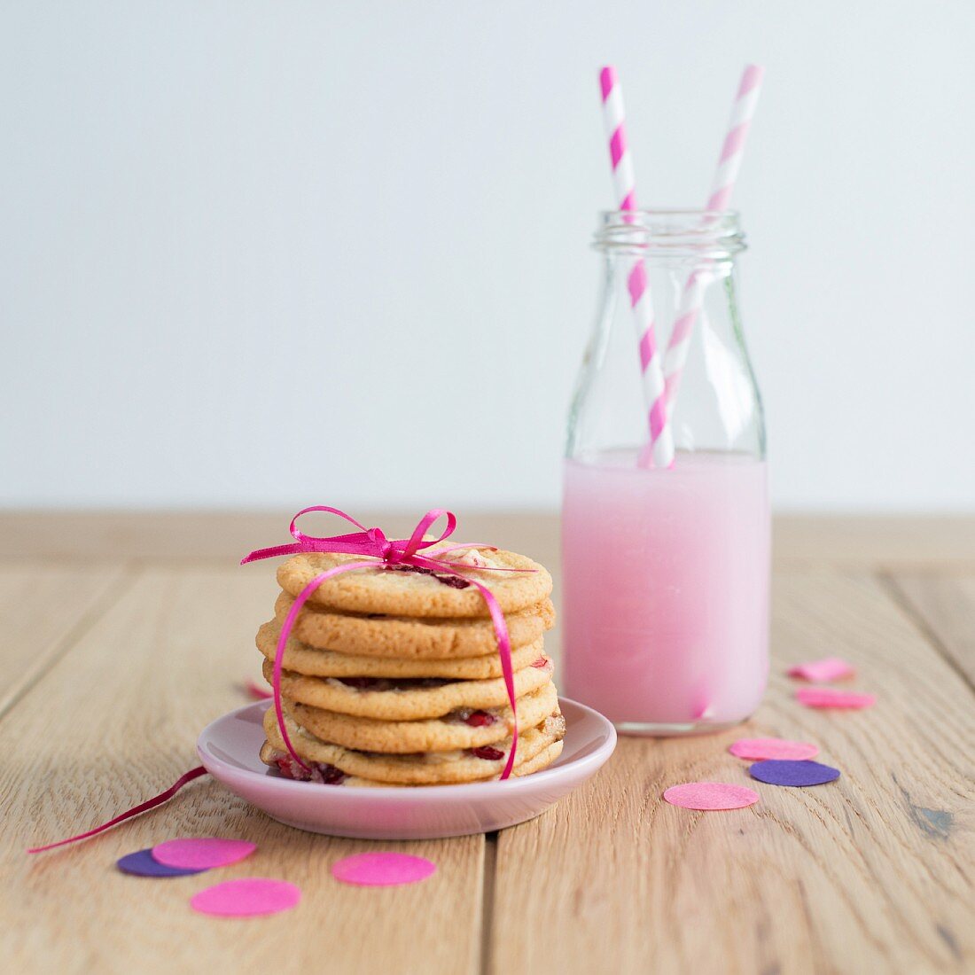 A stack of strawberry biscuits tied with ribbon with a strawberry drink