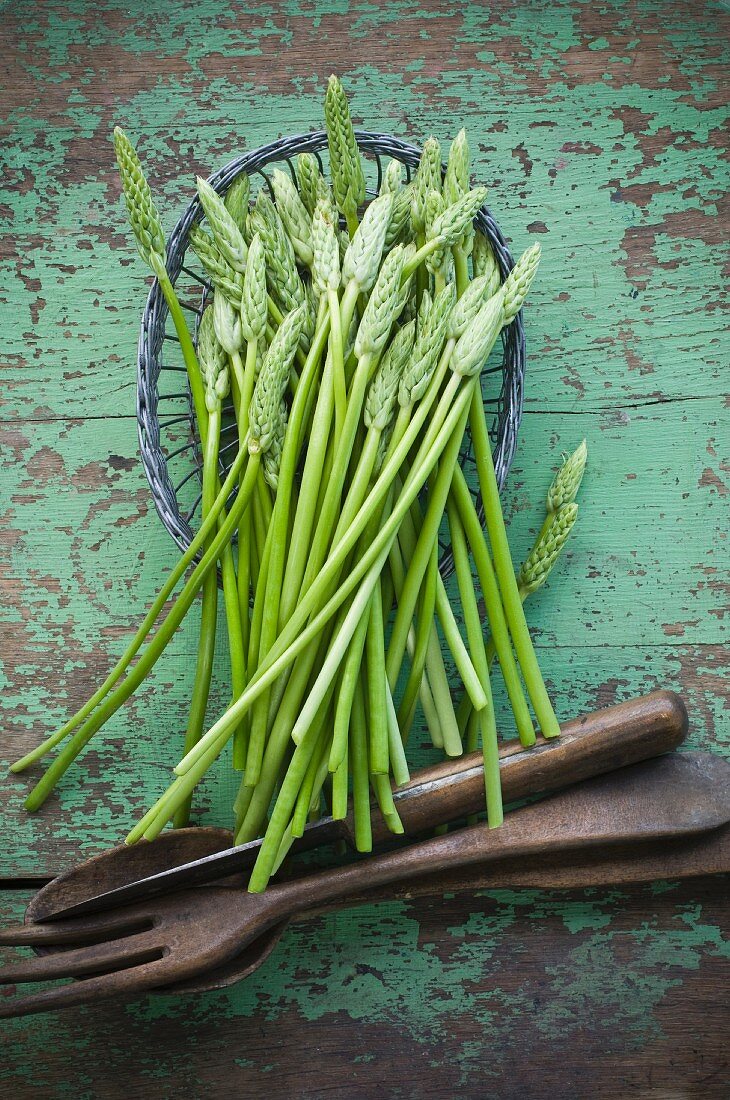 Wilder Spargel in einem Körbchen auf rustikalem Holztisch mit Salatbesteck