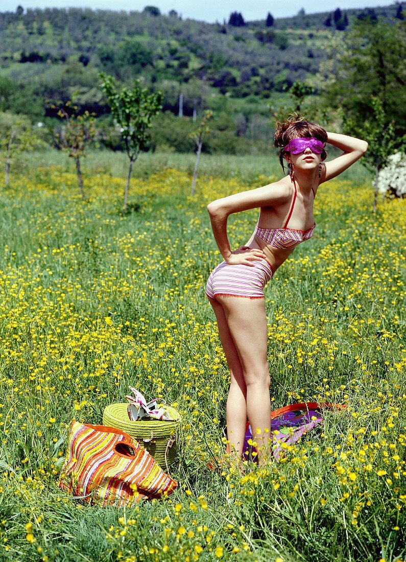 Junge Frau in Retro-Bikini mit Schlafmaske steht auf Blumenwiese