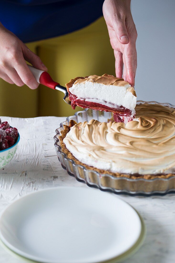 A woman slicing raspberry meringue tart