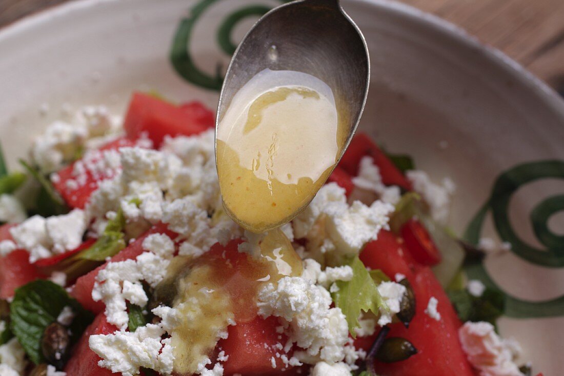 Dressing being poured onto a watermelon salad with feta cheese and mint
