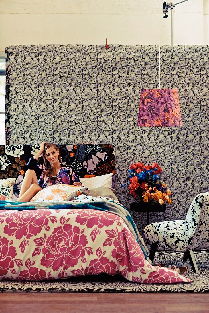 Young woman sitting on bed in room with different patterns