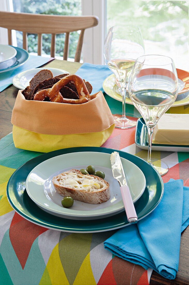 Gedeckter Tisch mit bunten Accessoires, Brot, Oliven und Weißwein