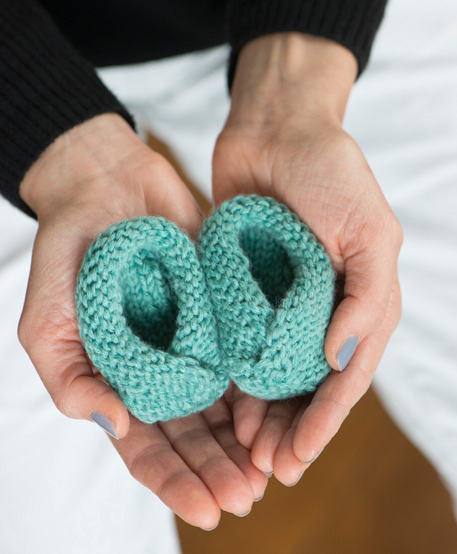 A woman holding knooked baby shoes – knitting with a hook