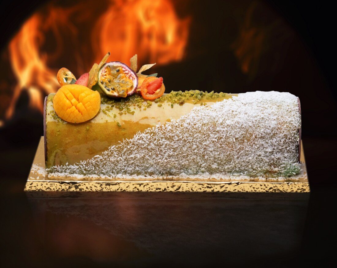 A Yule log with garnished with grated coconut and exotic fruit
