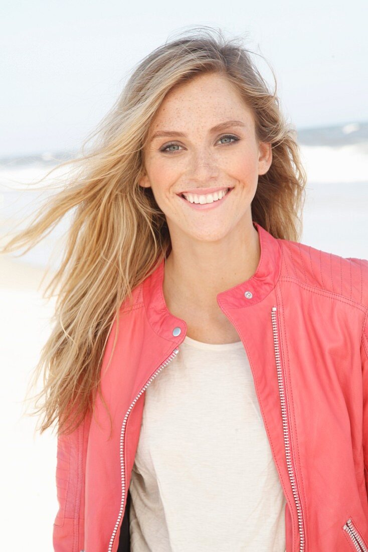 Young woman wearing pale T-shirt and salmon-pink leather jacket on beach