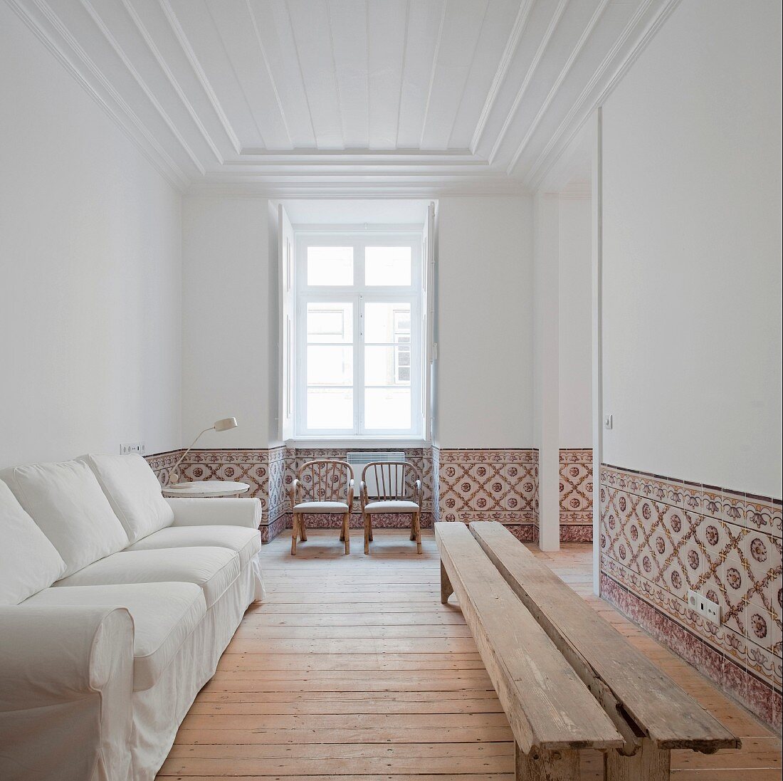 Weisses Sofa an Wand gegenüber rustikale Holzbank in weiße Wohnzimmer mit Wandfliesen in Brüstungshöhe
