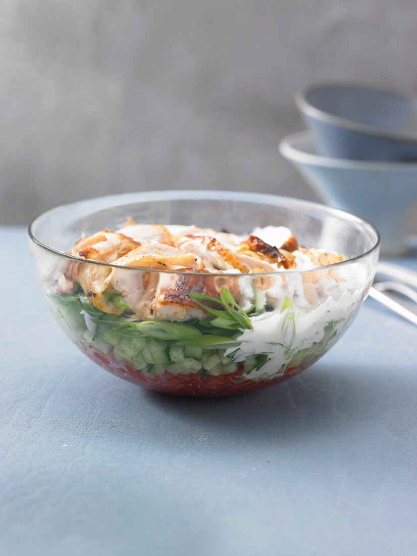 A layered salad with roast chicken, cucumber and tomatoes