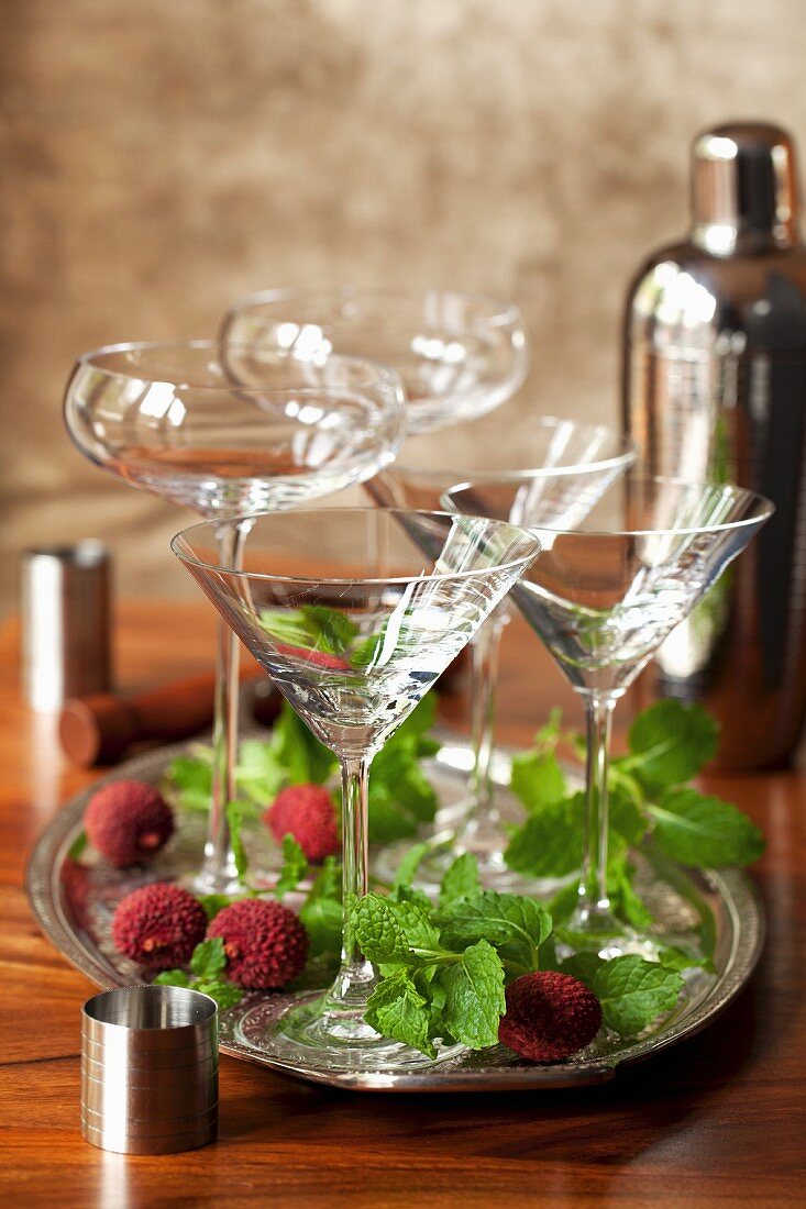Empty cocktail glasses on a tray surrounded by fresh mint and lychees