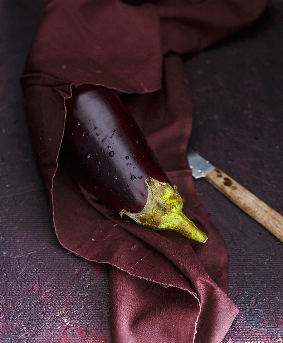 A freshly washed aubergine on a purple cloth