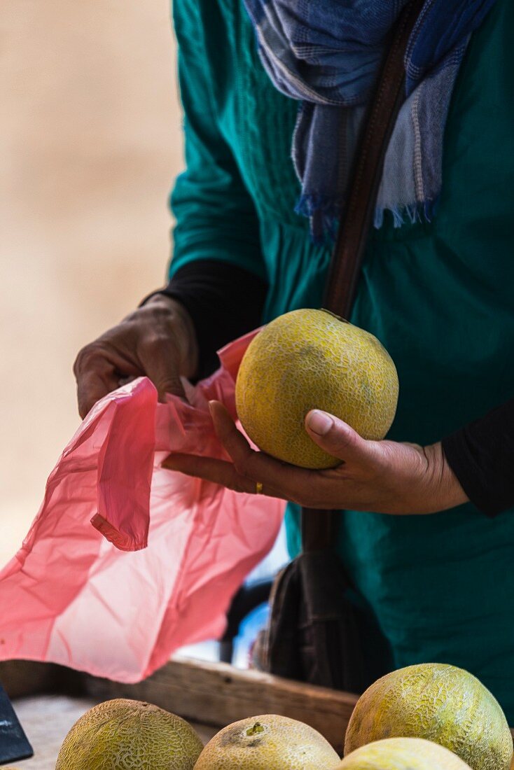 A woman choosing a melon at a market