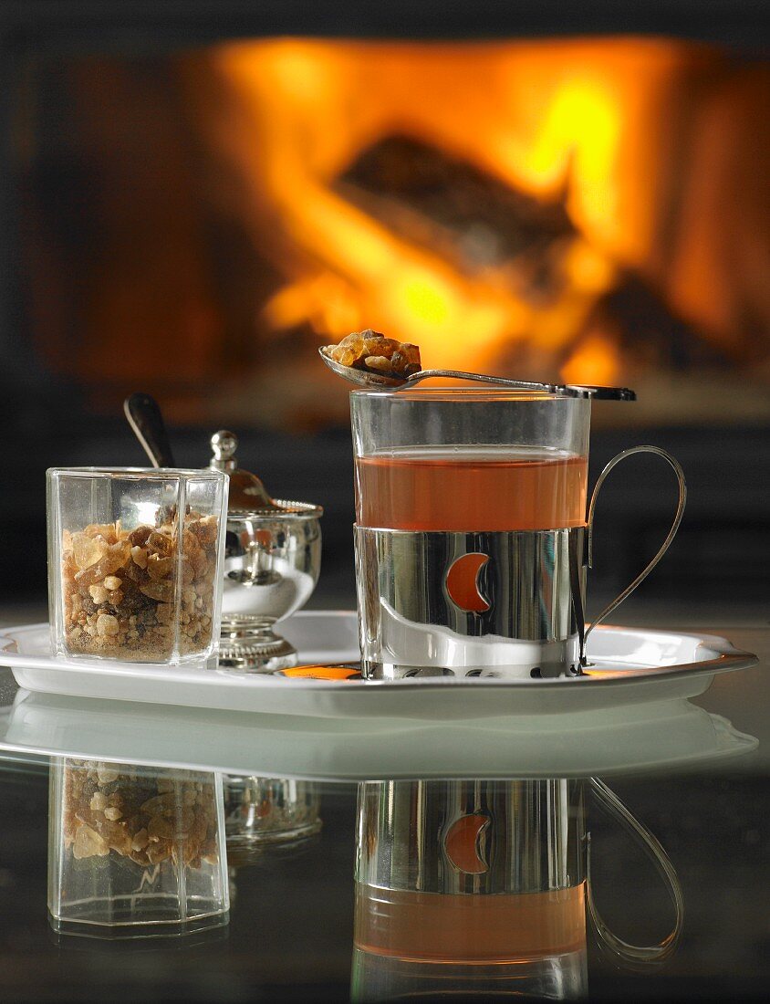 Heißer Tee mit Kandiszucker auf Tablett vor offenem Kamin