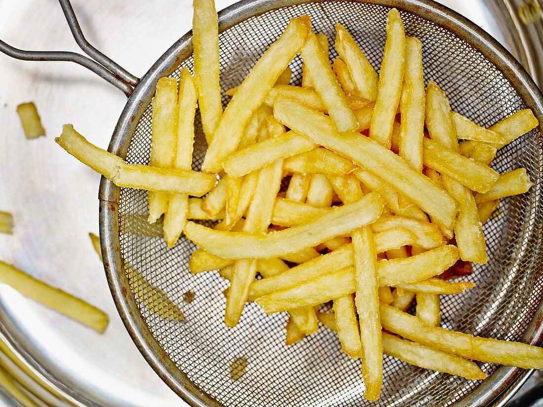 Frisch zubereitete Pommes frites im Sieb über der Abtropfwanne