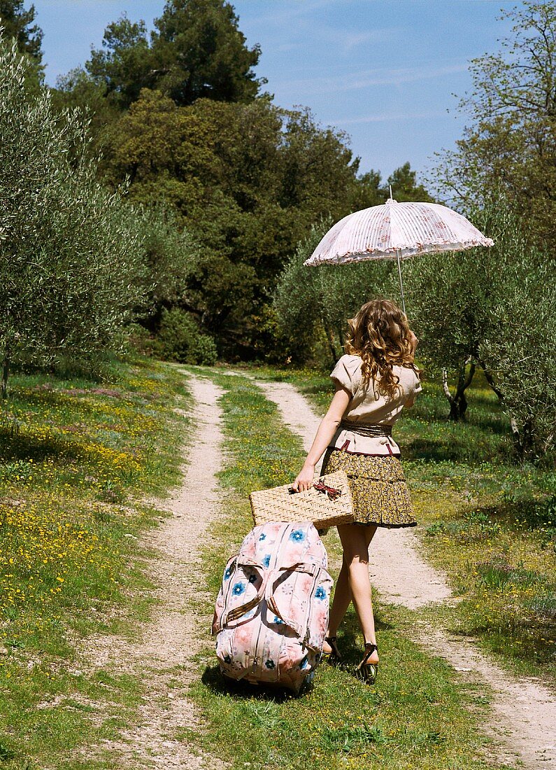 A young woman with a parasol and a holdall walking along a path