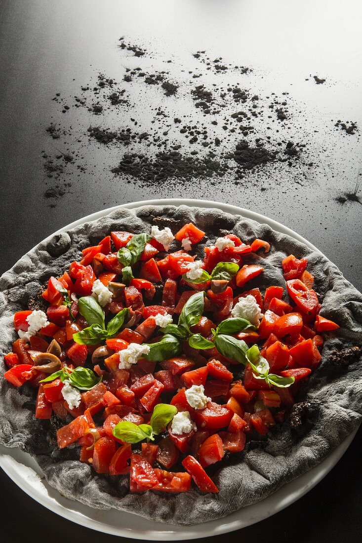 Schwarze Pizza mit Paprika, Tomaten, Oliven, Mozzarella und Holzkohlenpulver