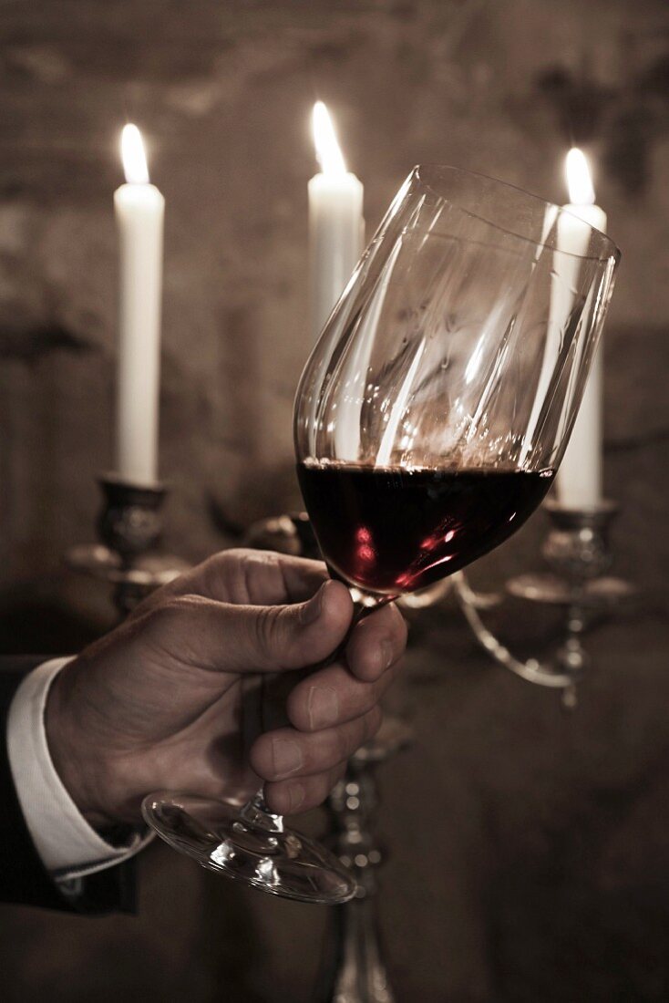 Christmas in a wine cellar: a hand holding a glass of red wine in front of a candelabra