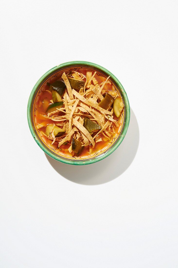 Spicy tortilla soup with chicken stock, tortilla strips, chicken, roasted vegetables and coriander