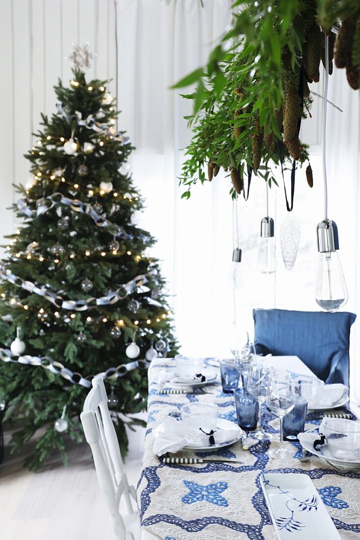 Christmas dinner table set in blue and white in front of Christmas tree