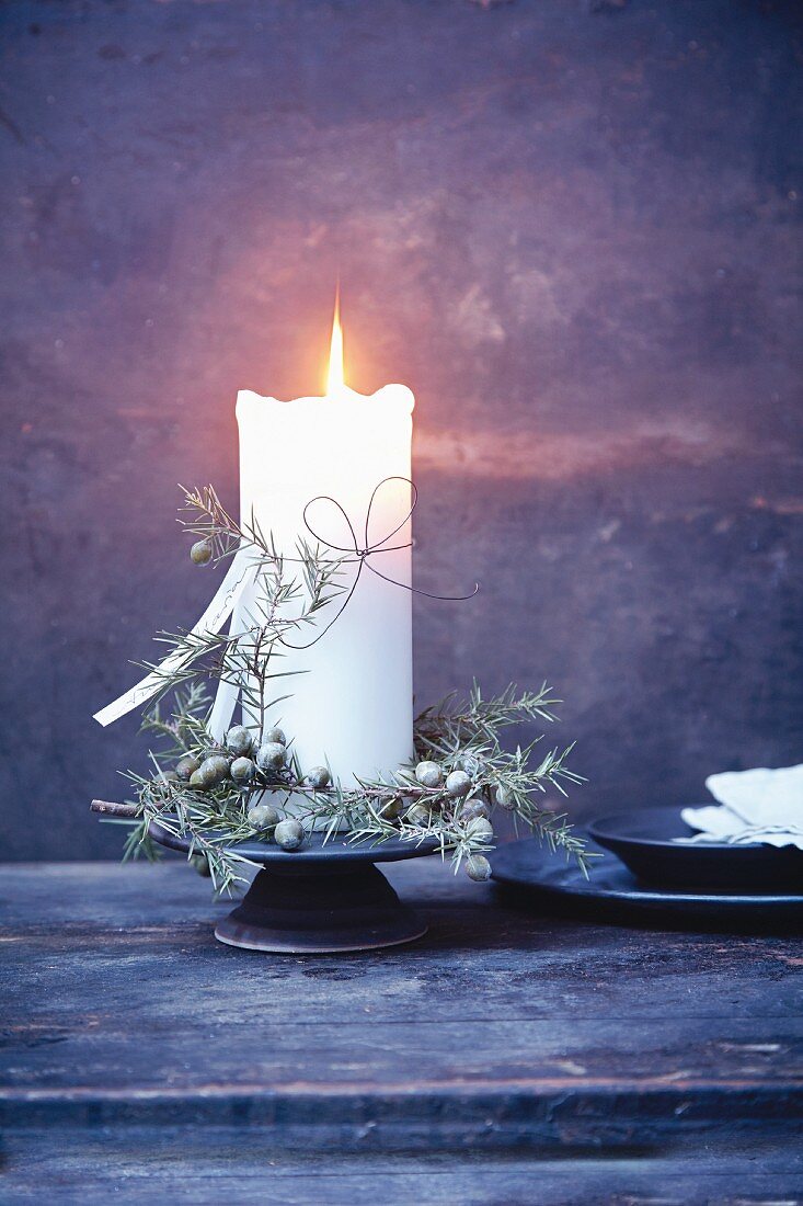 A candle holder decorated with a wreath of juniper berries