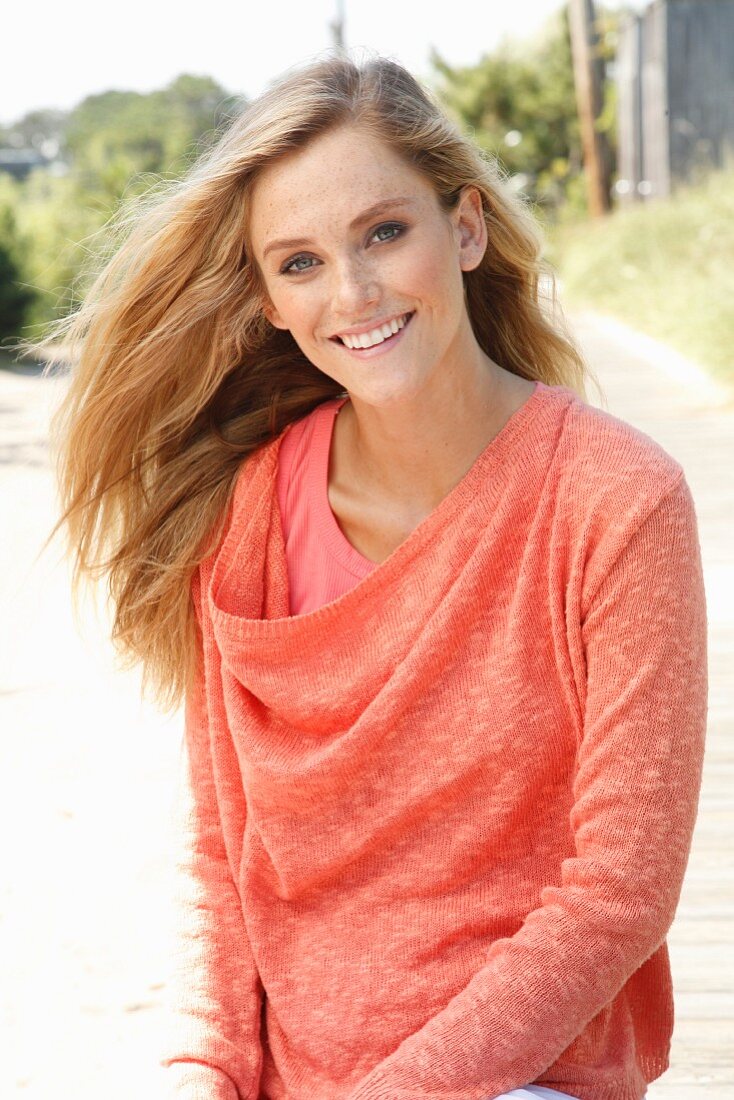 A blonde woman wearing a top and a salmon-pink knitted jumper