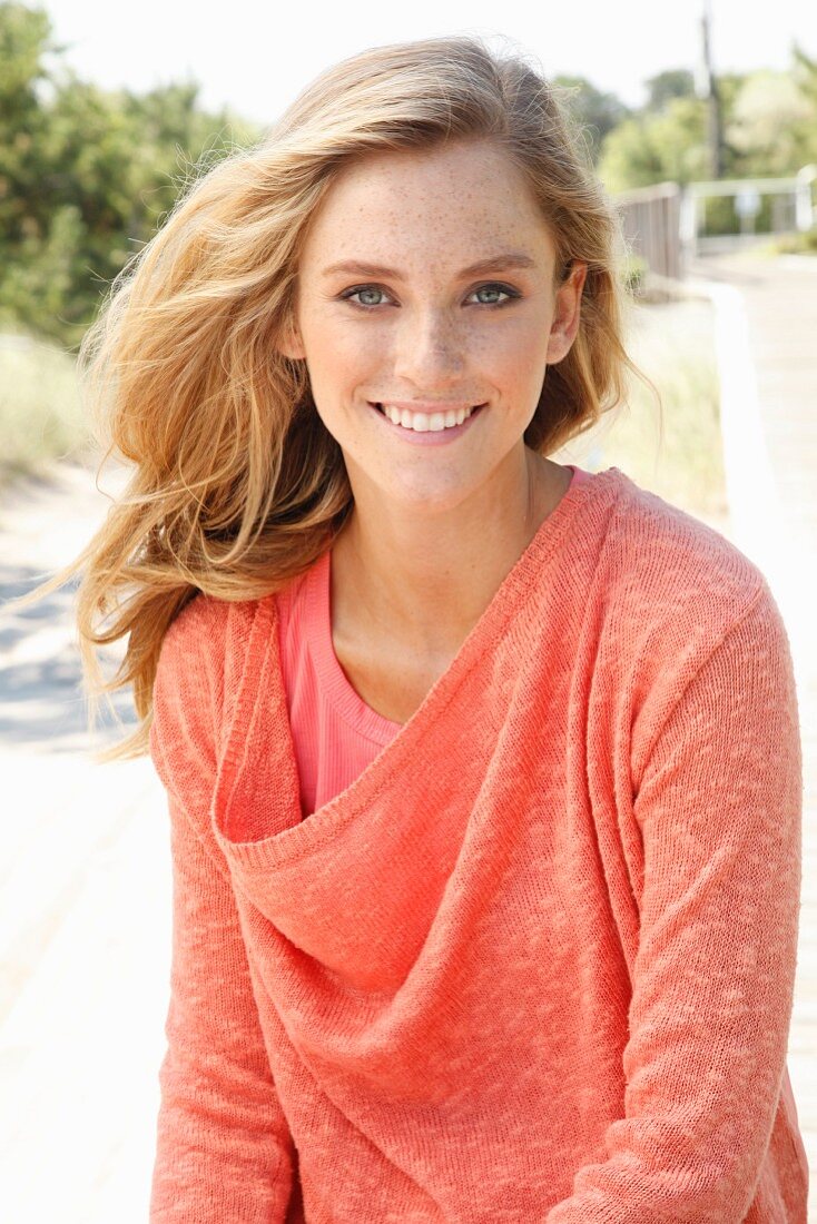 A blonde woman wearing a top and a salmon-pink knitted jumper