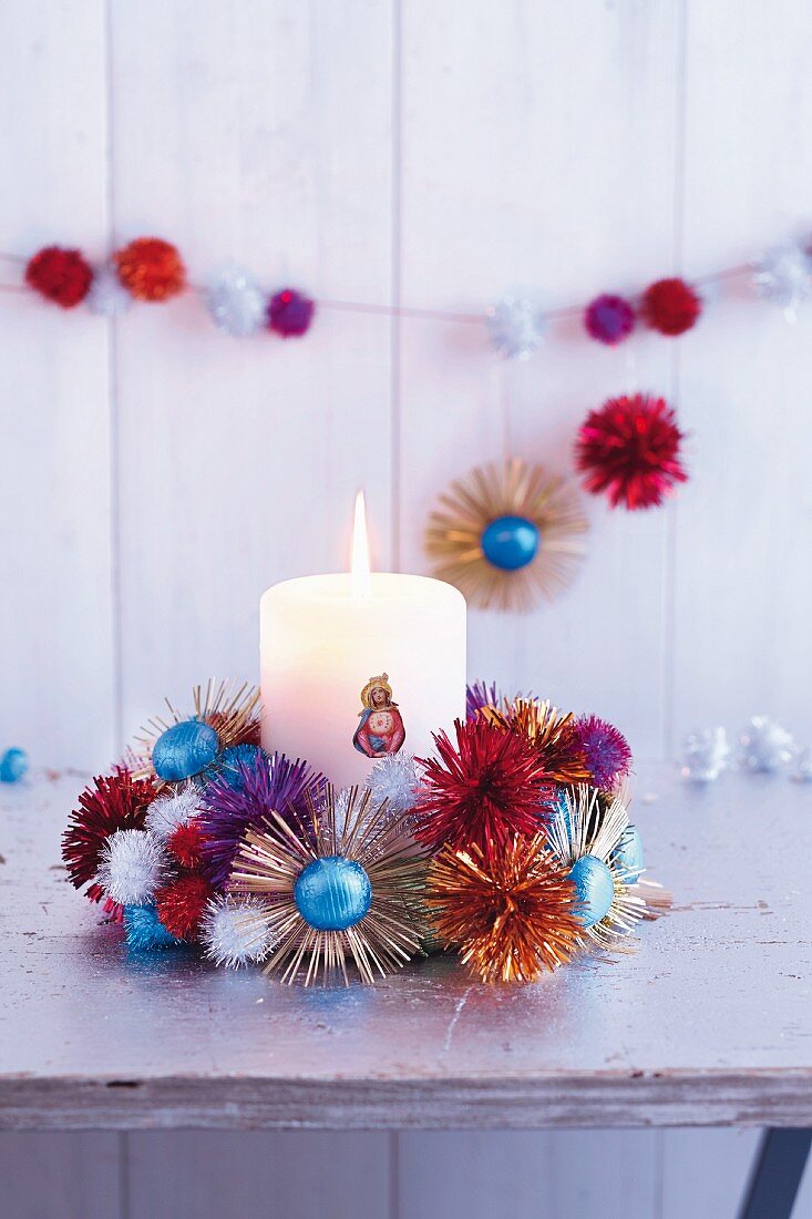 A brightly coloured glittery Advent wreath decorated with chocolate suns and glittery pompoms