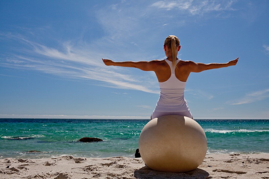 A woman practising yoga on a beach with an exercise ball